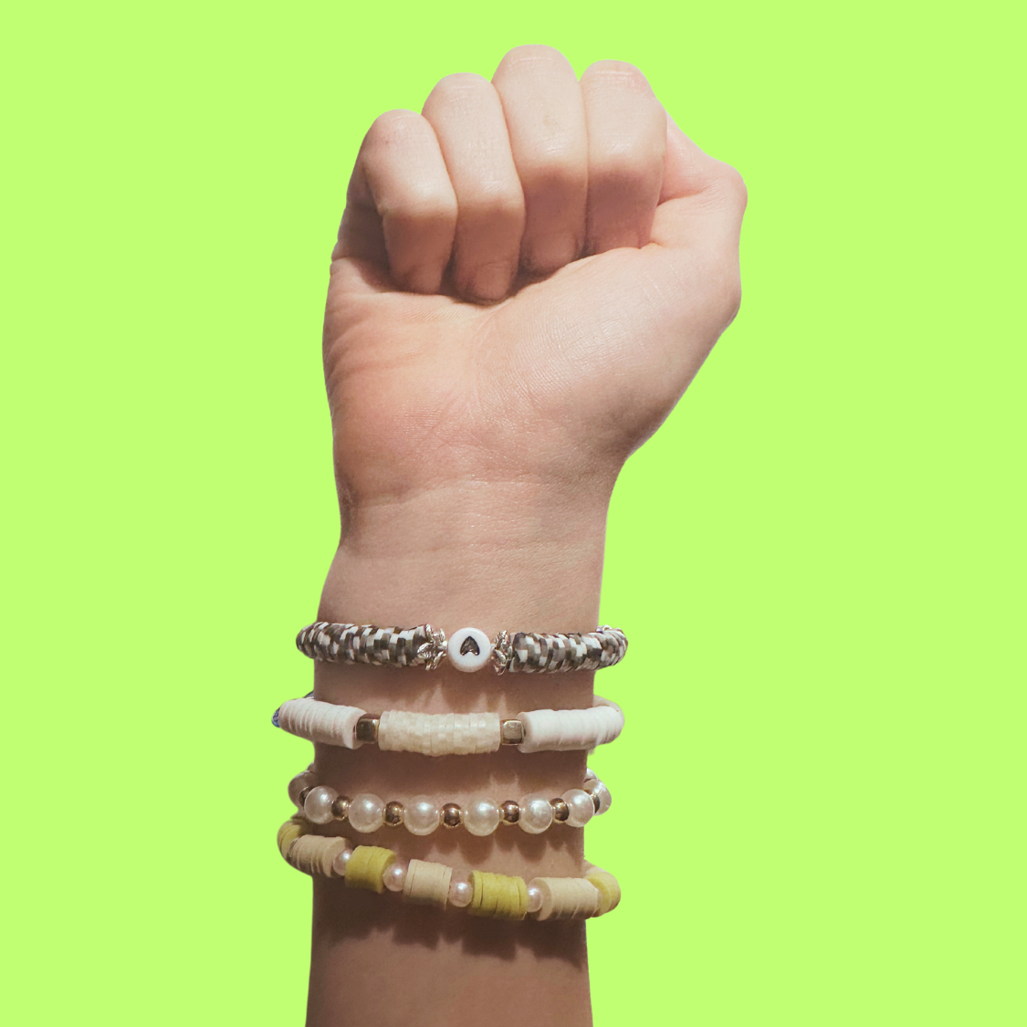 Stacked bracelets on a raised fist against lime green
