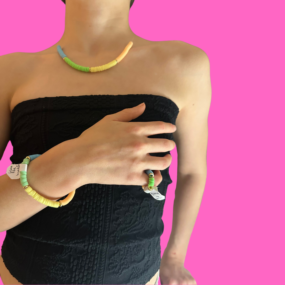 Colourful stacked bracelets and necklace on a pink background